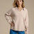 A woman wearing a light beige knit sweater with a split V-neck collar, paired with blue jeans, against a solid beige background.