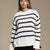 A woman wearing a cream knit sweater with horizontal navy stripes, photographed against a plain beige studio background.