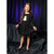 A young girl stands in a studio wearing a black long-sleeve dress with a white owl graphic on the chest. The background consists of draped black fabric with purple lighting.