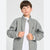 A young boy wearing a gray heather zip-up jacket with white striped cuffs over a white t-shirt, photographed against a light gray studio background.