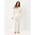 A woman modeling a two-piece pajama set with a long-sleeve button-up top and matching pants, featuring a delicate multicolor leaf pattern on a warm cream background, set against a plain white studio backdrop.