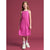 A young girl with long light brown hair stands against a solid dusty rose pink studio background, wearing a sleeveless bright pink midi dress, white socks, and white sneakers.