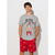 A man modeling a heather gray graphic t-shirt and red patterned shorts against a light gray studio background. The t-shirt features a cartoon graphic of a tattooed man wearing a Santa hat with the text 'BIG NICK IS BACK TO TOWN'.