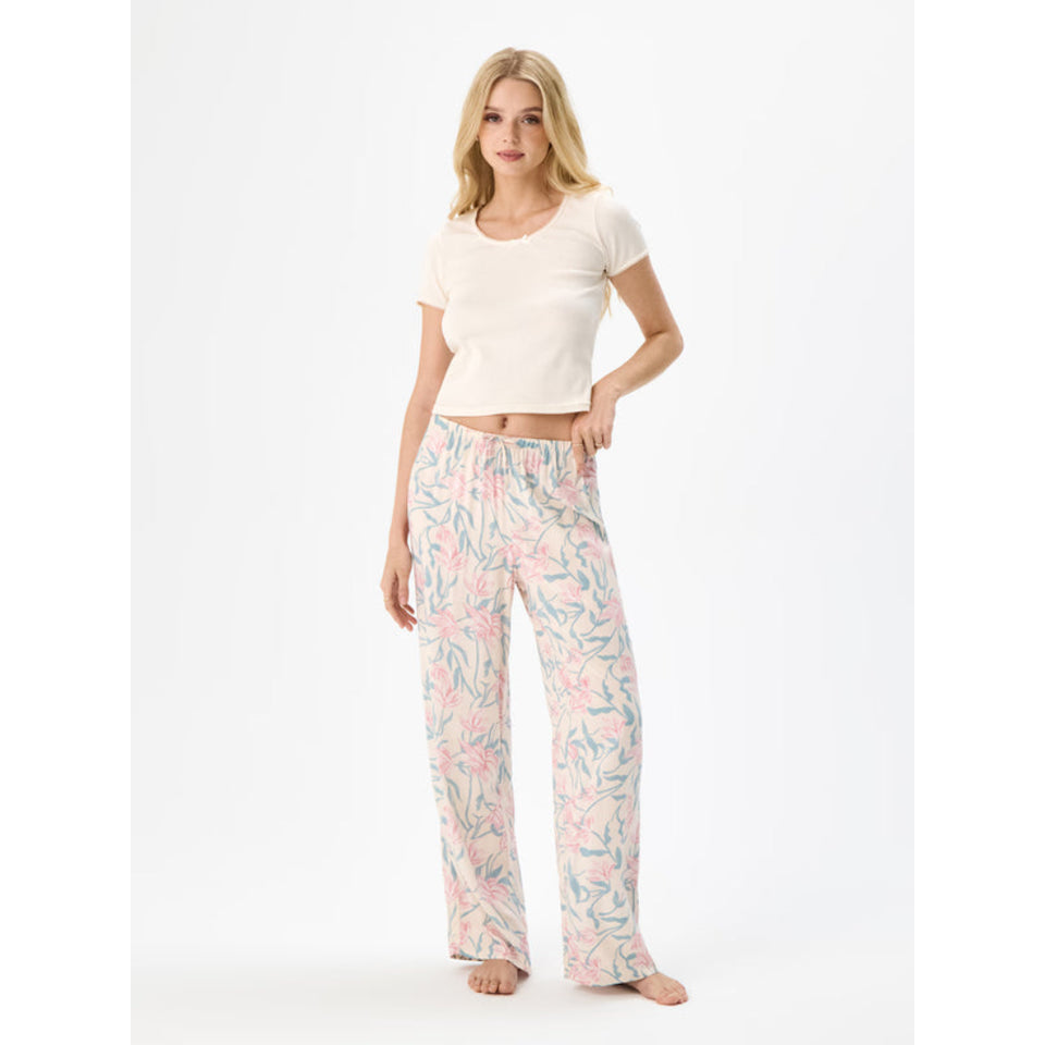A woman modeling a two-piece pajama set consisting of a cream short-sleeve crop top and matching wide-leg pants with a pink and teal botanical leaf pattern, set against a plain white studio background.