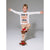 A young boy posing in a white long-sleeve t-shirt with a 'Cookie Baking Crew' graphic and beige patterned pajama pants, balancing on one foot while wearing gingerbread-themed slippers against a gray studio background.