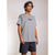 A man wearing a light gray oversized crewneck t-shirt with a small dark gray graphic on the left chest, paired with dark navy shorts, standing against a light gray studio background.