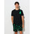 A man modeling a black short-sleeve t-shirt with a green tree-shaped hanging ornament graphic on the chest, paired with black shorts featuring a green tree pattern, set against a plain light gray background.