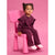 A toddler girl wearing a matching textured burgundy corduroy two-piece outfit with ruffle sleeves, sitting on a bright pink plastic chair against a solid pink background.