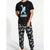 A man modeling a black short-sleeve t-shirt and matching black jogger pants with white dinosaur patterns. The t-shirt features a graphic of an astronaut carrying a moon and the text 'DEMONAUT JOURNEYS'.
