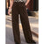 A person wearing dark brown wide-leg trousers, standing outdoors on a sidewalk with one hand in a leopard-print top.