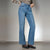 A model wearing a pair of high-waisted, straight-leg blue denim jeans with a faded wash, styled with a zebra-print long-sleeve top and black studded flats against a neutral studio background.