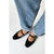 Black Mary Jane flats with gold-tone buckle details, shown on a model wearing light-wash blue jeans against a plain white background.