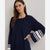 A woman wearing a navy blue knit cardigan with wide bell sleeves featuring white stripes on the cuffs, posed against a neutral light gray background.