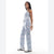 A woman modeling a sleeveless light blue and white floral print jumpsuit, paired with white sneakers, against a plain white studio background.