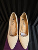 Pair of beige pointed-toe shoes with brand logo on a dark background