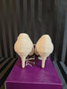 Pair of beige high-heeled shoes on a purple platform with a black and gray striped background.