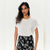 A woman modeling a white short-sleeve crewneck t-shirt paired with black and white floral print pants, set against a plain off-white background.