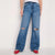 A person wearing blue wide-leg distressed jeans with ripped knee details, paired with a white top and red shoes, standing against a plain light background.