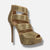 A single gold platform high-heeled sandal covered in sparkling rhinestones, featuring an open toe, ankle strap, and multiple cutaway straps, shown on a light gray background.