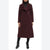 A woman wearing a long, dark burgundy wool coat over a black turtleneck and black ankle boots, shown against a plain white background.