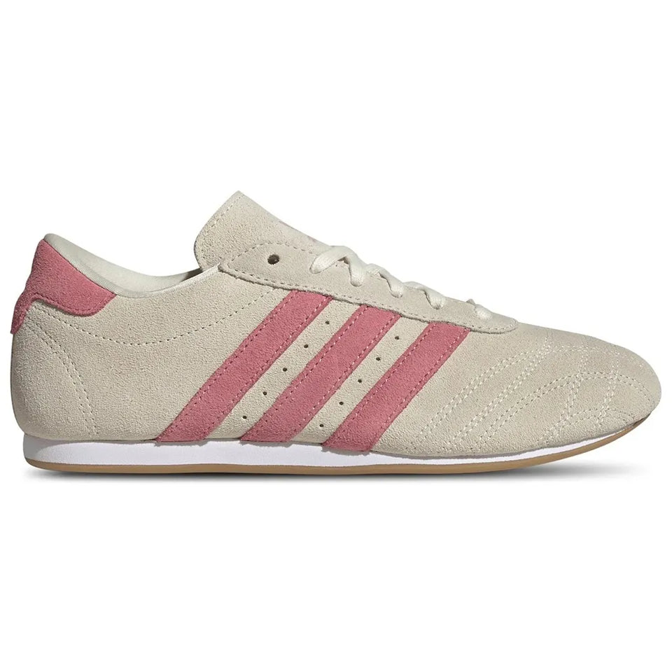 A classic low-top sneaker in beige suede and mesh with three pink stripes, a pink heel tab, and a white midsole.