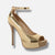 A metallic gold high-heeled pump with an ankle strap, open toe, and platform sole embellished with rhinestones, shown against a light gray background.