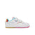 A white Reebok kids' sneaker with colorful rainbow line details, hook-and-loop strap closures, a metallic gold heel tab, and a pink outsole, shown against a plain white background.