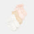 Four pairs of baby ankle socks in white, beige, light pink, and pale peach, arranged diagonally on a light gray background. Each pair features a delicate lace ruffle at the top.