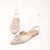 A pair of pointed-toe slingback flats in a light nude beige satin, embellished with a clear rhinestone sunburst flower on the toe and a transparent strap, shown on a clean off-white background.
