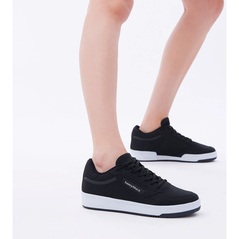 A person wearing black low-top sneakers with white midsoles, shown from the calves down against a clean white studio background. The brand name 'Lompiask' is visible on the side of the front shoe.