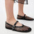 Black fishnet Mary Jane flats with a glossy strap and silver buckle, shown on a model's feet against a white background.