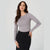 A woman modeling a fitted, long-sleeve crewneck top in a light gray color, paired with a black skirt, against a plain light gray studio background.