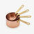 A set of nested copper measuring cups with gold-colored handles and engraved measurements including 1/4 cup, 1/3 cup, 1/2 cup, and 1 cup, shown on a clean white background.