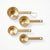 A set of five nested measuring cups in brushed gold metal, arranged diagonally on a clean white background.