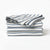 A stack of folded striped fabric napkins or table linens in blue-gray and off-white, photographed on a clean white studio background.