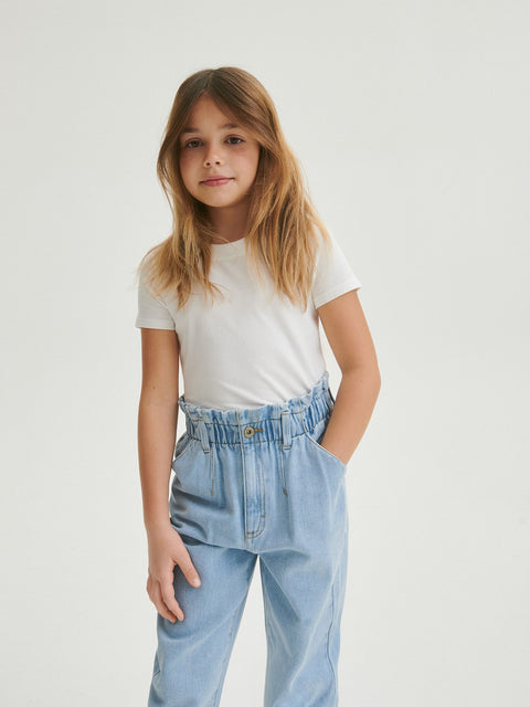 Young girl wearing a white t-shirt and light blue jeans on a plain background