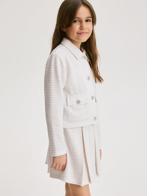 Young girl wearing a white blazer and skirt set on a plain background