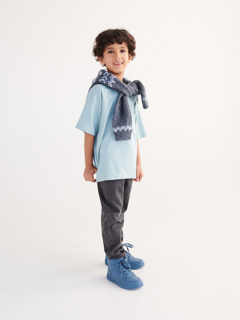 Child wearing a light blue shirt, dark gray pants, and blue shoes with a patterned scarf on a white background