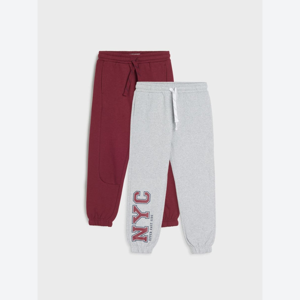 Two pairs of jogger sweatpants shown flat against a light gray background: one pair is heather burgundy with a drawstring waist and cuffed ankles, and the other pair is heather light gray with a white drawstring and a large vertical 'NYC' graphic on the leg.