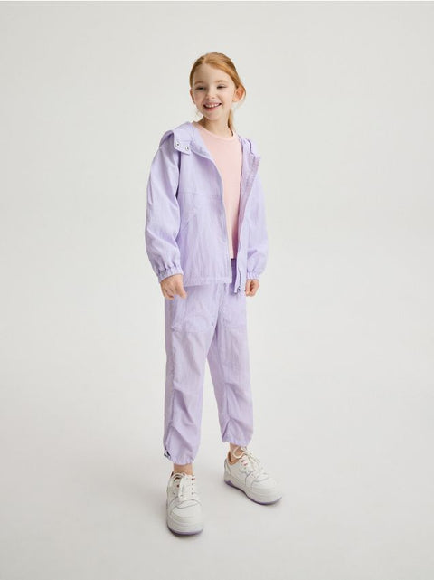 Young girl wearing a light purple tracksuit on a white background
