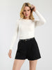 Woman wearing a white ribbed sweater and black shorts on a light gray background