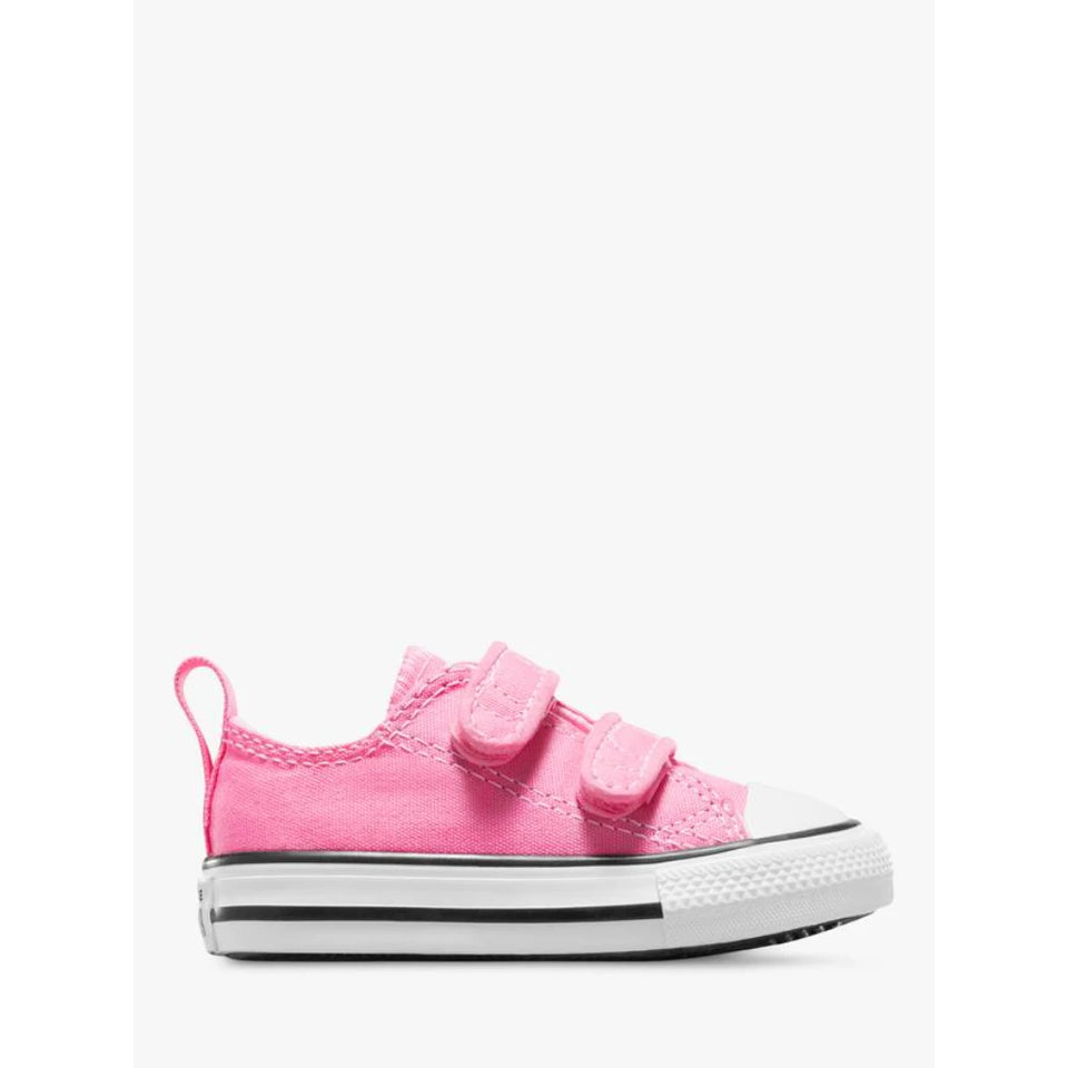 A pink canvas low-top sneaker with two hook-and-loop straps, a white rubber toe cap, and a white midsole with a black stripe, shown in profile against a light gray background.