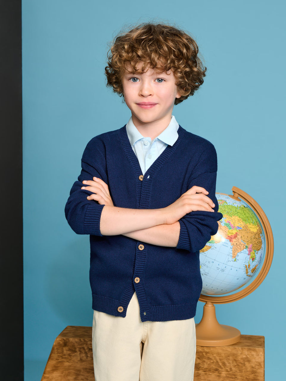 Child wearing a navy blue cardigan with a globe in the background