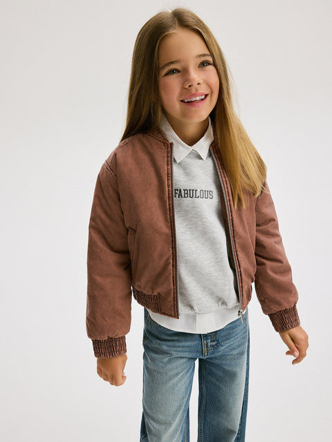 Young girl wearing a brown jacket over a 'Fabulous' shirt on a white background