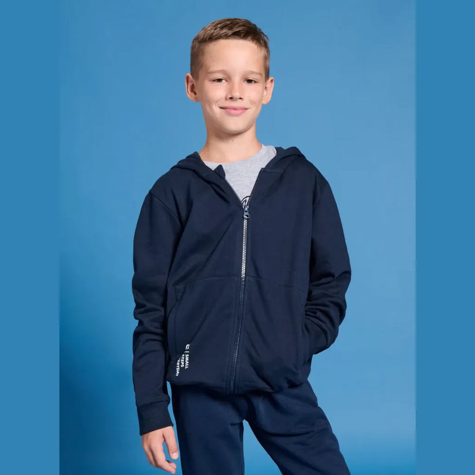 A young boy wearing a navy blue zip-up hoodie and matching sweatpants over a gray t-shirt, standing against a blue studio background.