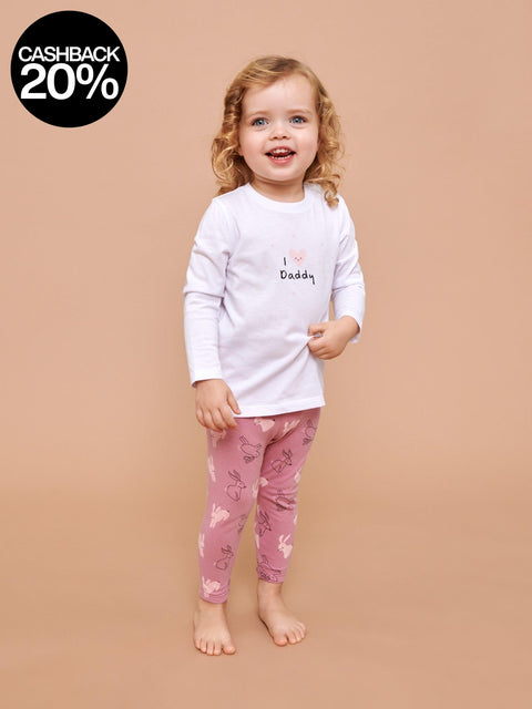 Child wearing a white long-sleeve shirt and pink pants with heart patterns on a beige background