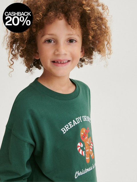 Child wearing a green sweatshirt with Christmas-themed design on a plain background
