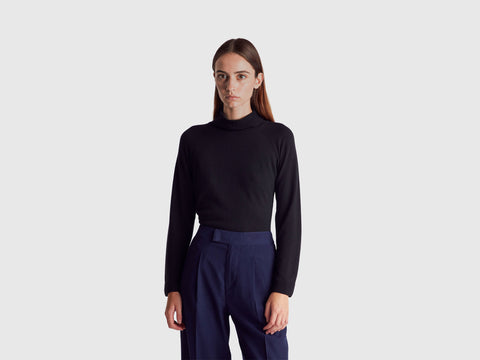 Person wearing a black turtleneck and navy pants on a white background