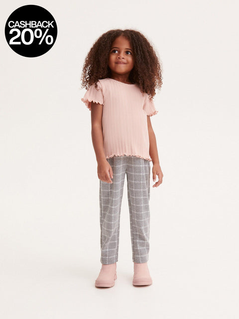 Young girl wearing a pink top and gray checkered pants on a white background