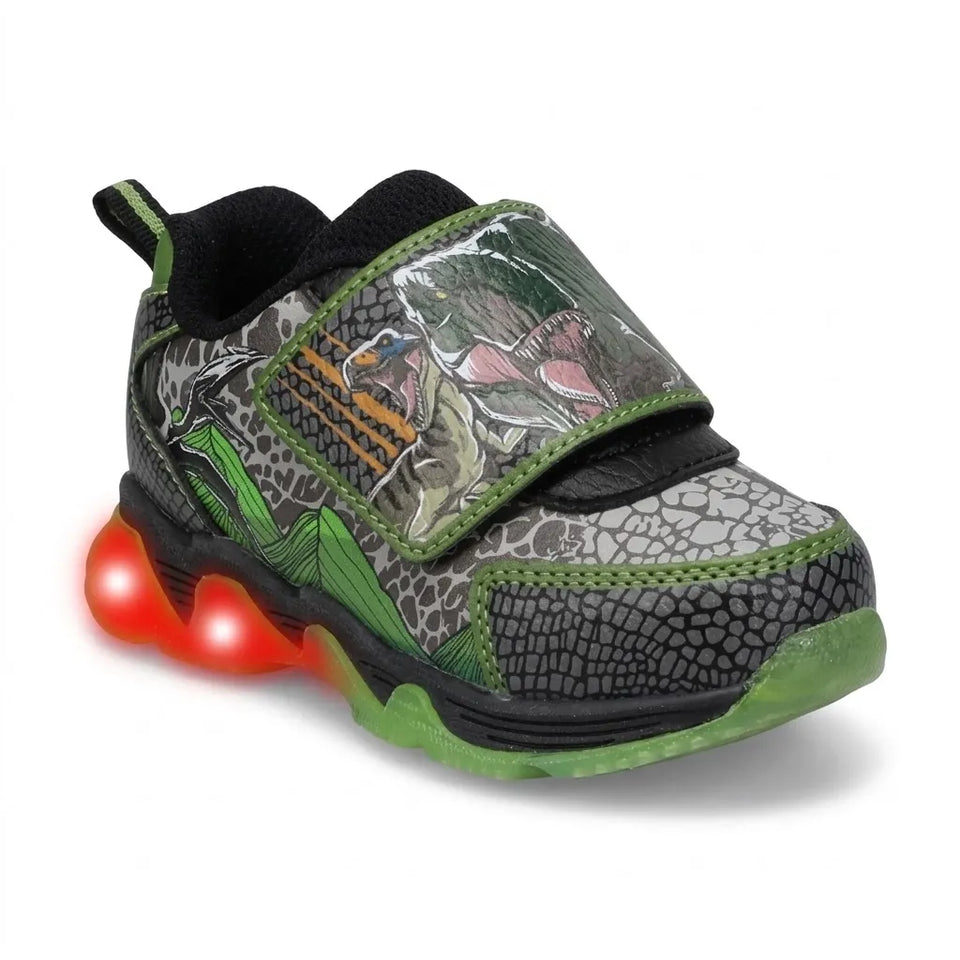 A toddler's light-up sneaker featuring a dinosaur-themed camouflage pattern in green, gray, and black, with a glowing red LED sole and a hook-and-loop strap closure.